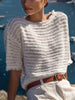Simi fringe-trim knit pullover in off-white, styled with a brown leather belt and cream trousers by the water