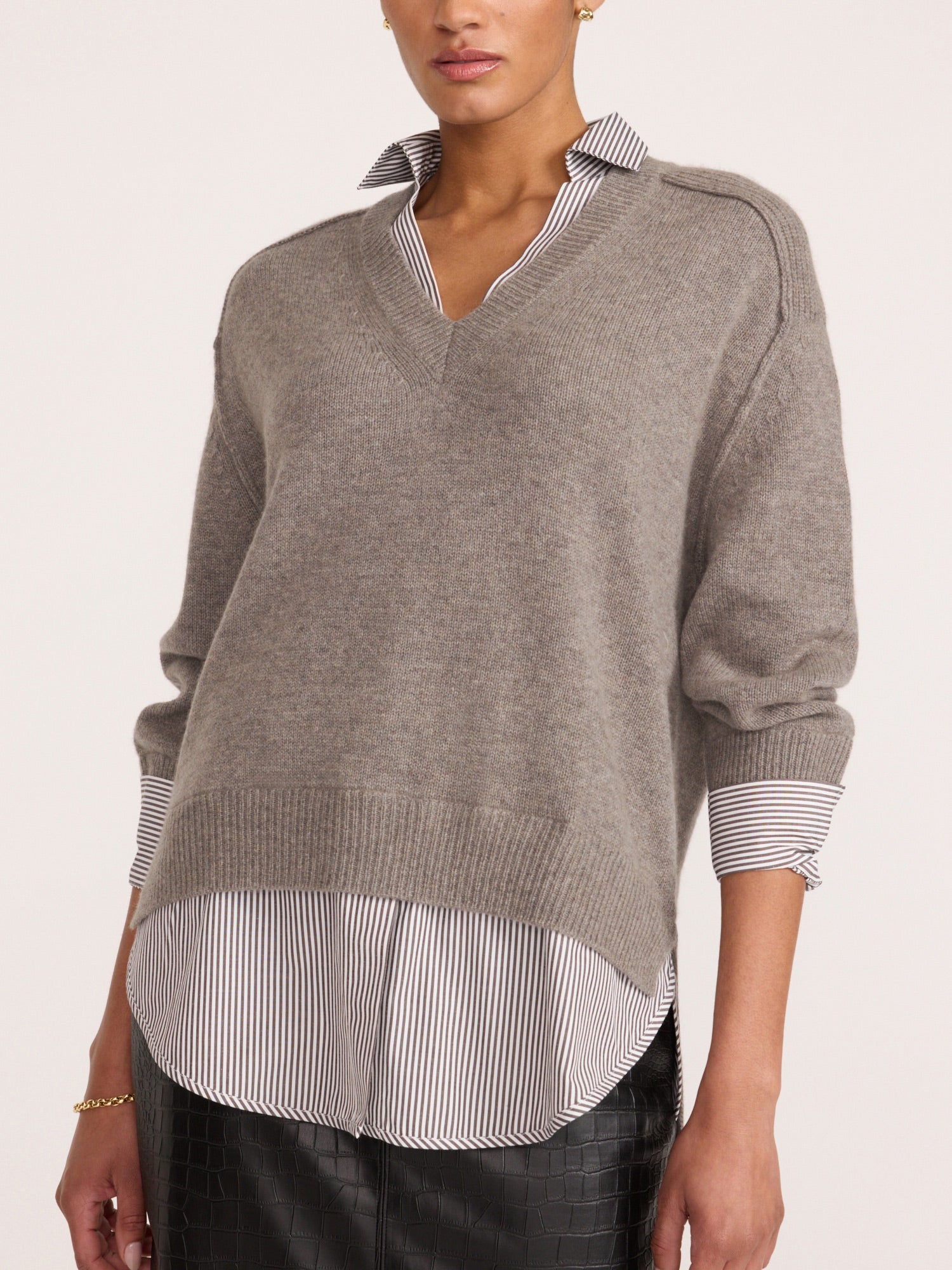 Woman wearing the pullover v-neck sweater in otter melange with flint stripe, layered over a striped button-down shirt with textured black pants.