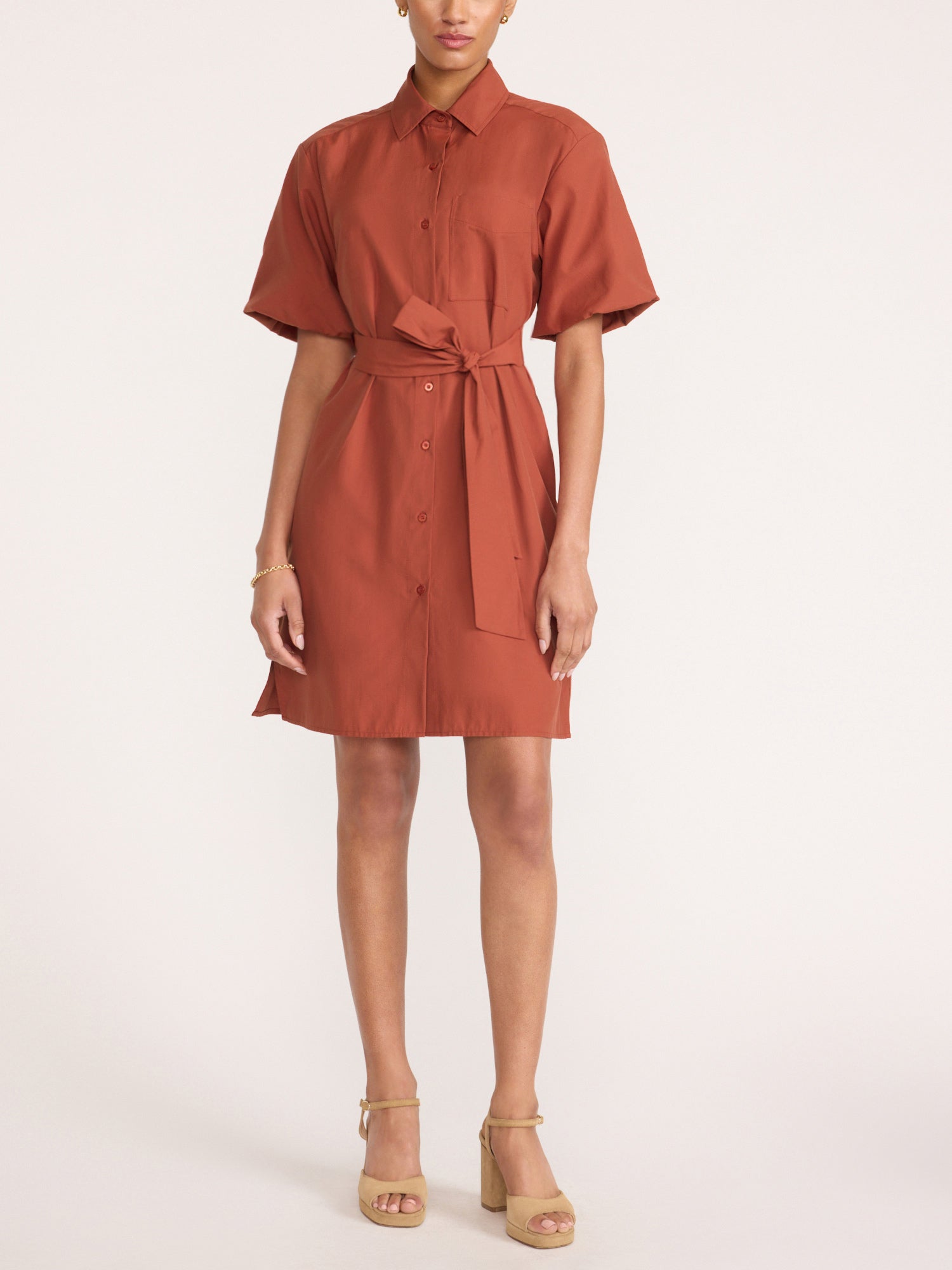 Woman wearing the Villa dress in Tuscany, a short-sleeve shirt dress with a waist tie, paired with beige strappy heels.