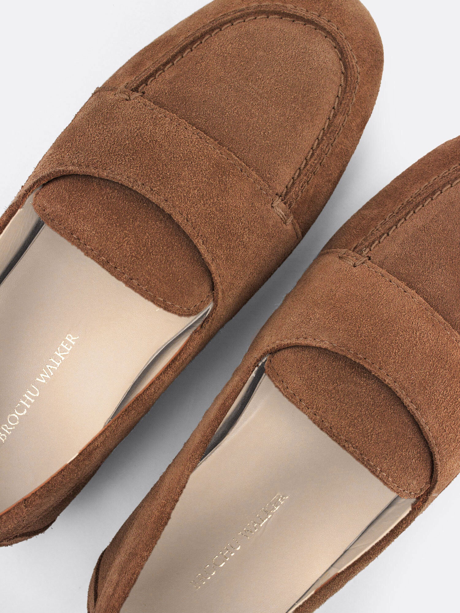 Close-up of tan suede loafers showing the branded leather insole detail.