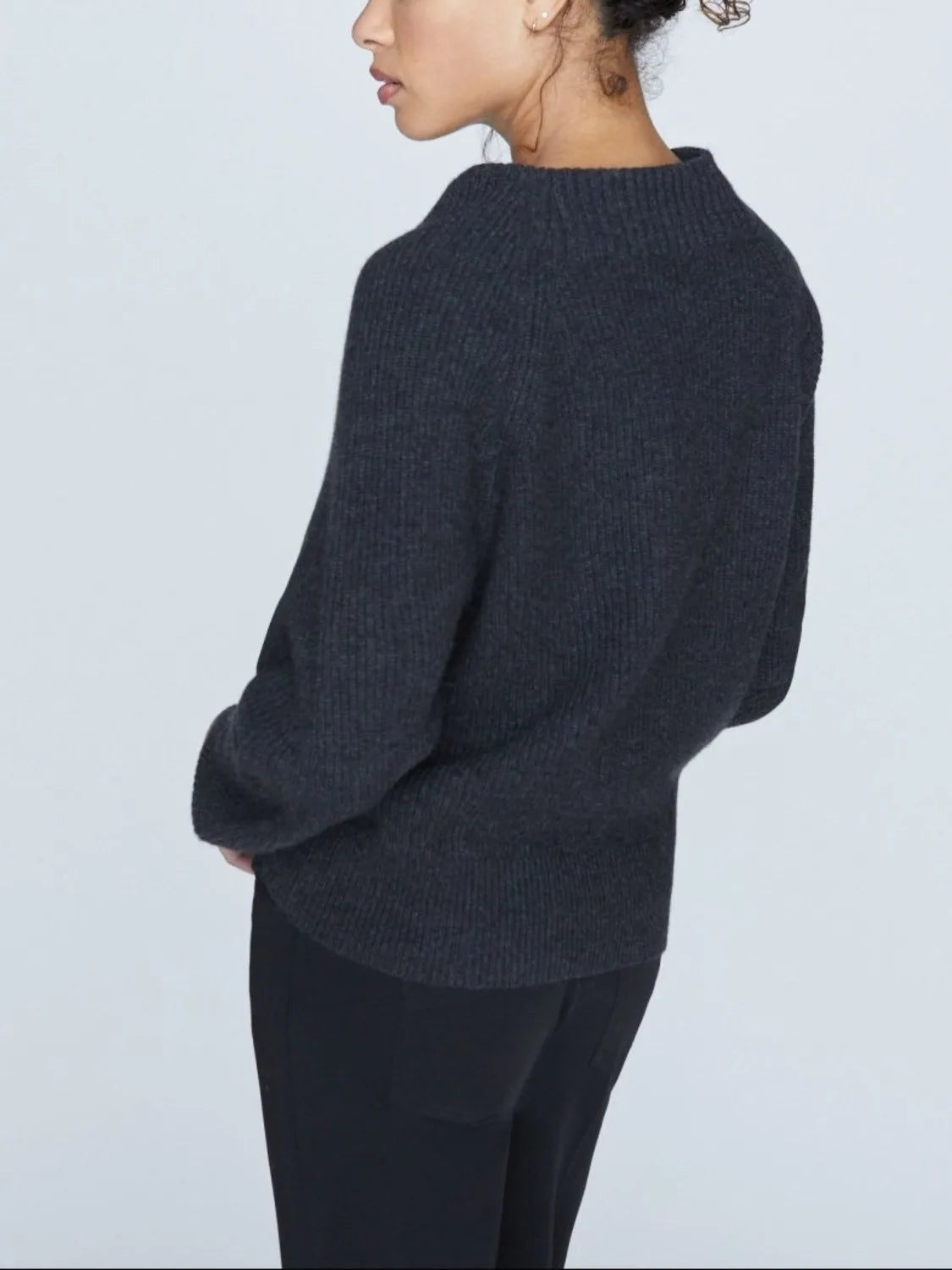 Back view of charcoal ribbed cashmere sweater with cowl neckline, worn with black pants.