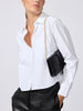 Close-up of a black crocodile-embossed clutch bag on a gold chain strap, worn over a white button-down shirt and black leather trousers.
