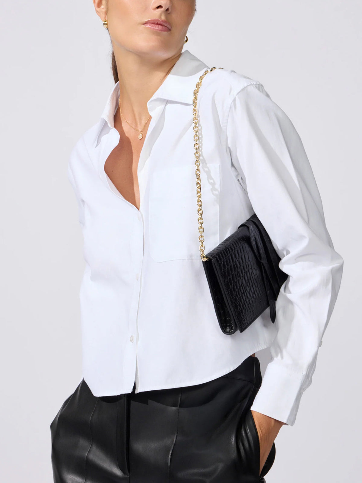 Model wearing a crocodile leather shoulder pochette on a gold chain strap with a white shirt and black leather pants