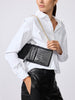 Woman in a white button-down shirt carrying a black crocodile-embossed clutch bag with a gold chain strap.