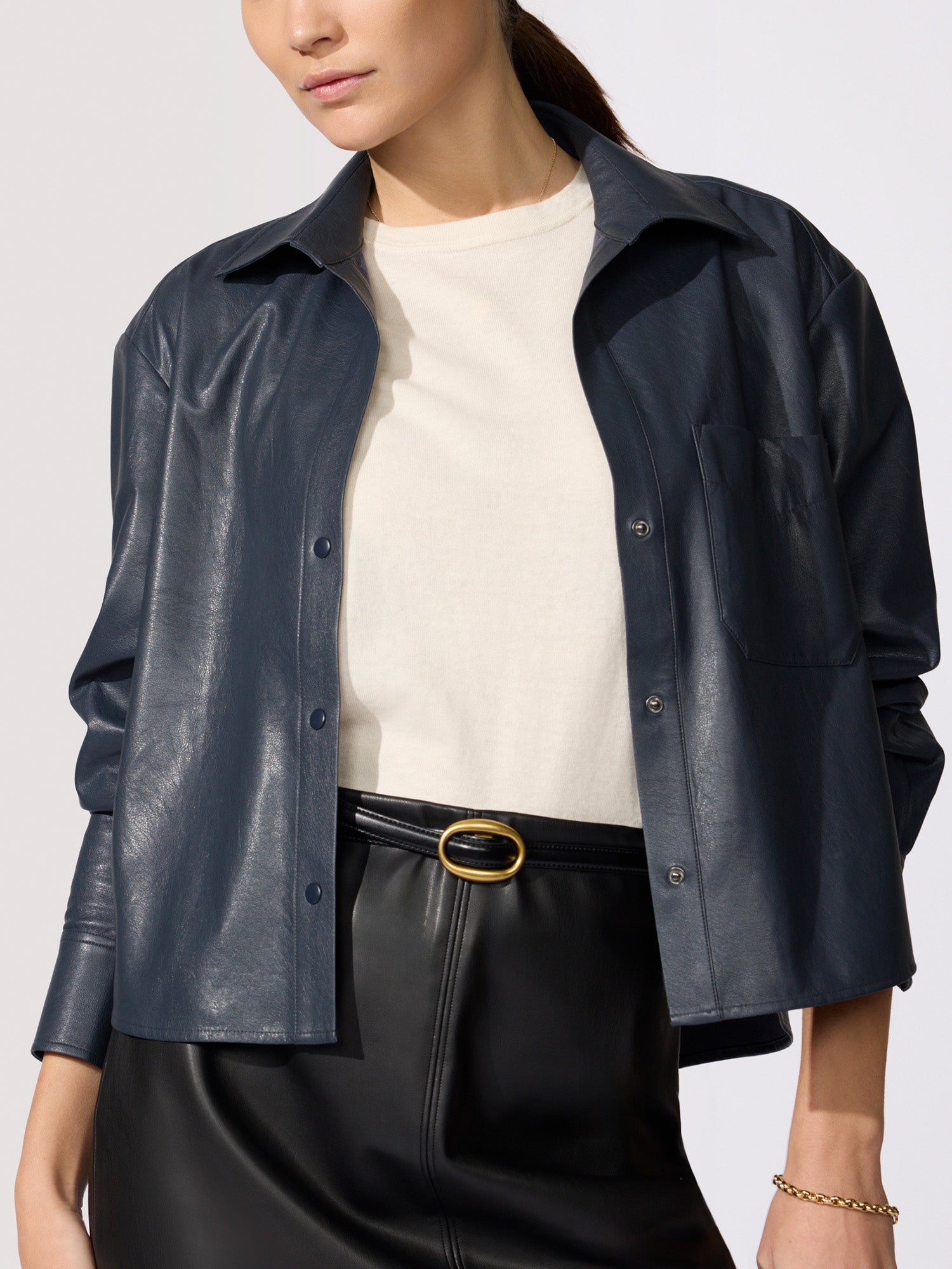 Cropped vegan leather shirt jacket in navy, layered over a cream top with a black leather skirt and gold belt