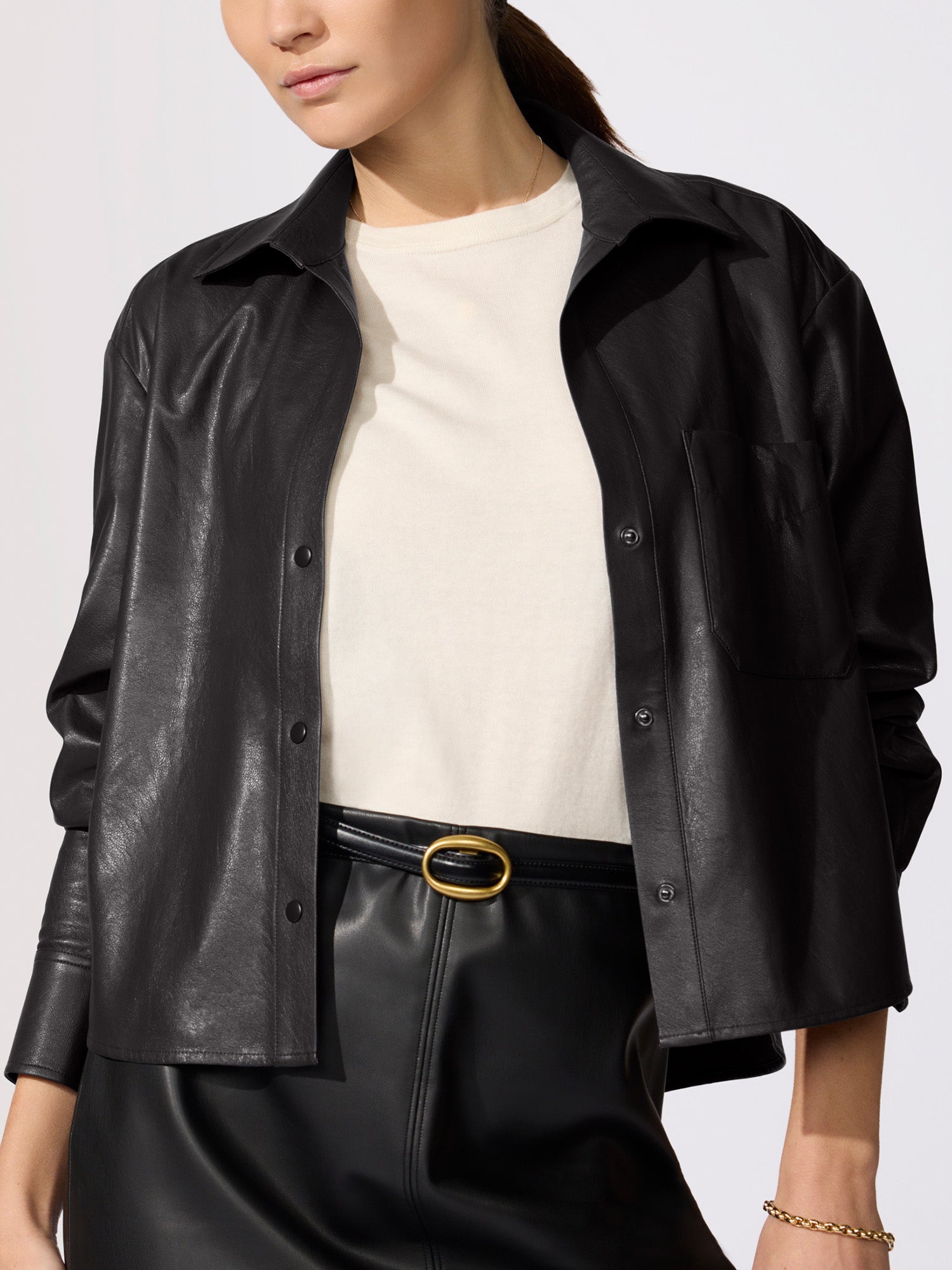 Cropped vegan leather shirt jacket in black, layered over a cream top with a black leather skirt and gold belt