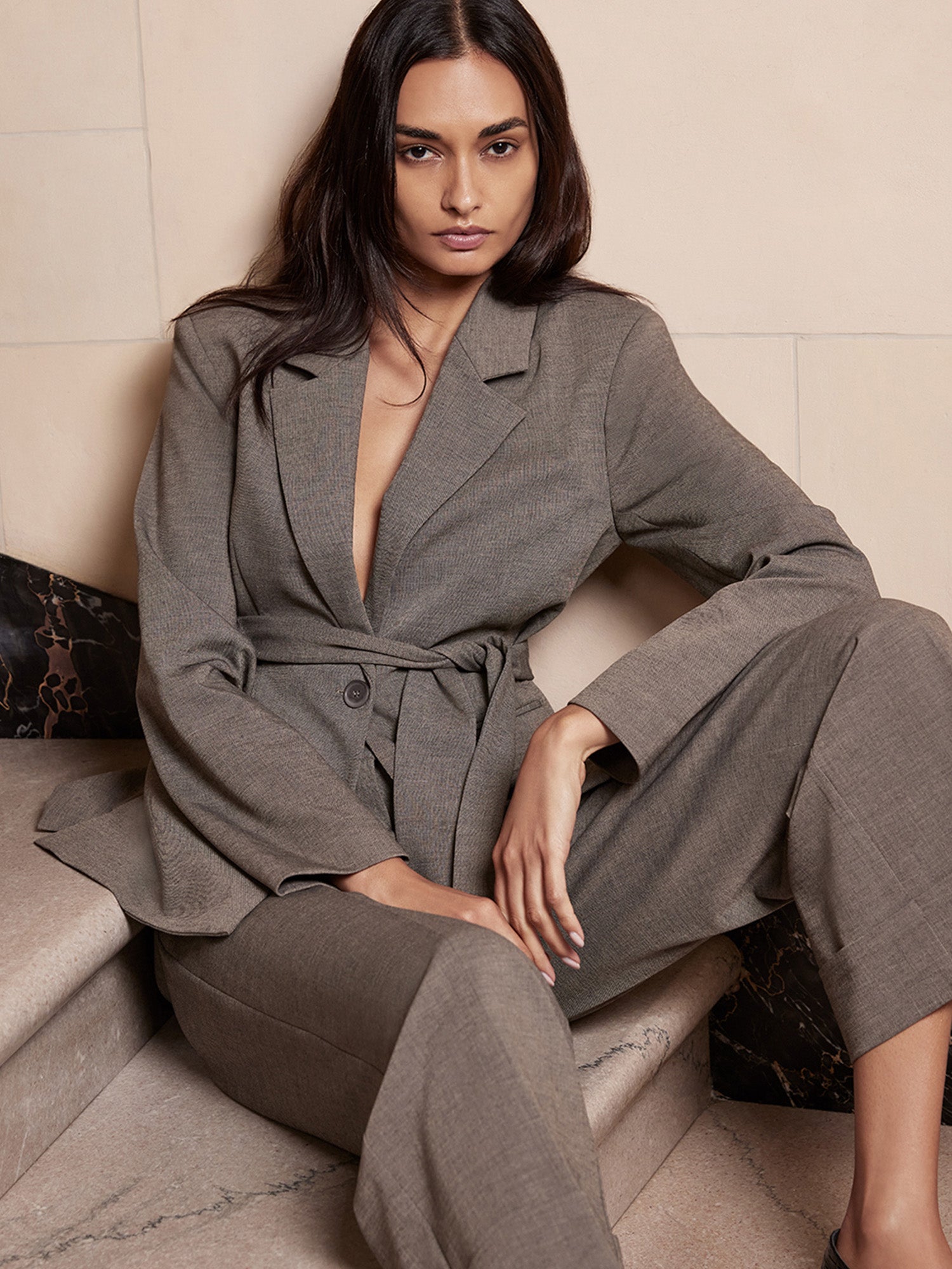 Belted blazer and wide-leg trouser set in taupe gray, close-up seated portrait on stone steps