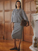 Woman wearing a gray cropped knit cardigan and matching midi skirt set with a brown suede bag