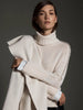 Model wearing a cream turtleneck layered sweater with white satin cuffs and a draped wool wrap.