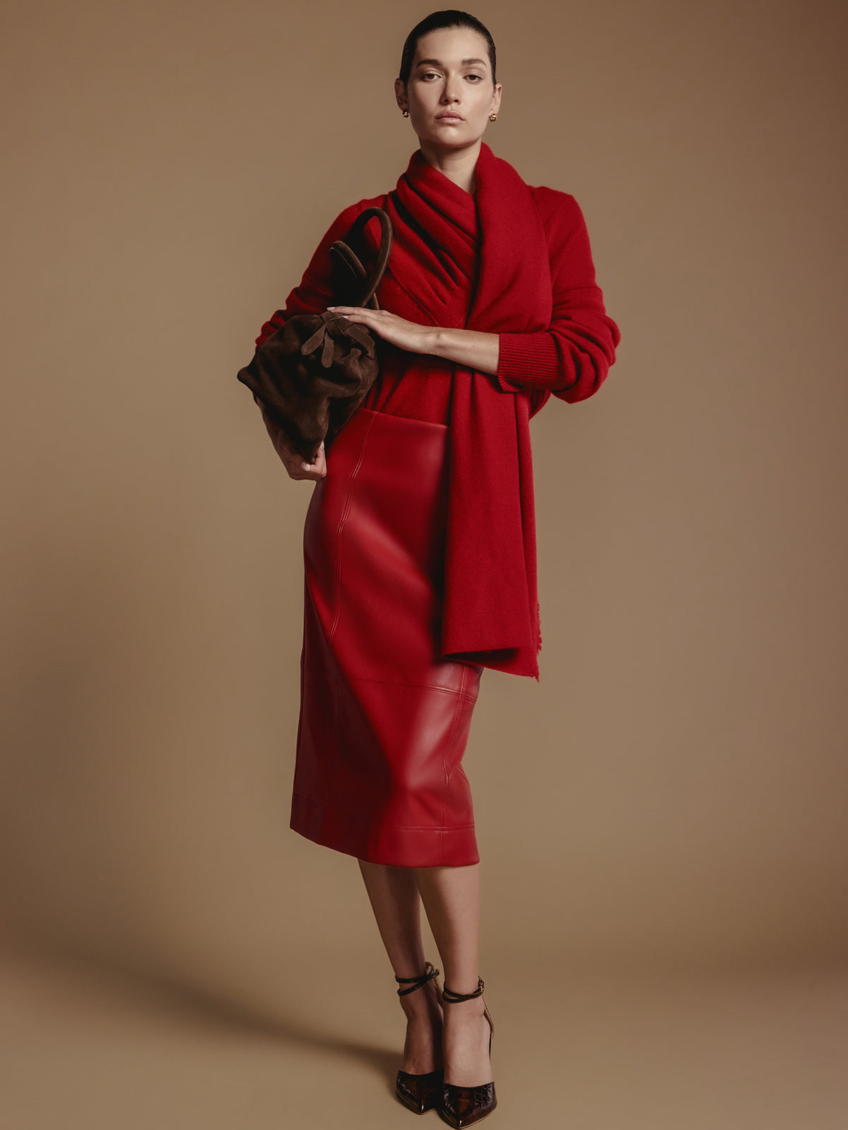 Front view of a women's red leather midi skirt, styled with a gray sweater, a gold bracelet and black ankle-strap heels