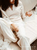 Person in a cream layered V-neck sweater and white pants lounging with a glass of rosé.