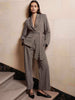 Woman modeling a gray belted blazer and matching wide-leg trousers, paired with black pointed-toe flats on stone steps.