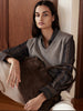 Woman seated indoors wearing a gray knit sweater vest over a striped button-up shirt, holding a brown suede tote bag.