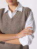 Person with arms crossed wearing a taupe knit sweater vest over a white collared shirt.