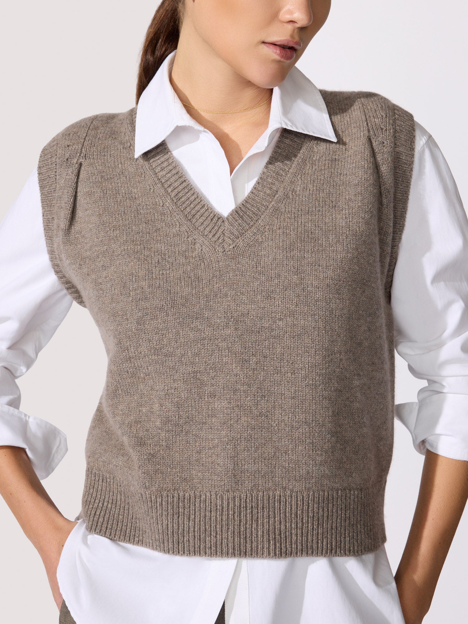 Close-up of a taupe V-neck knit sweater vest layered over a white collared shirt.
