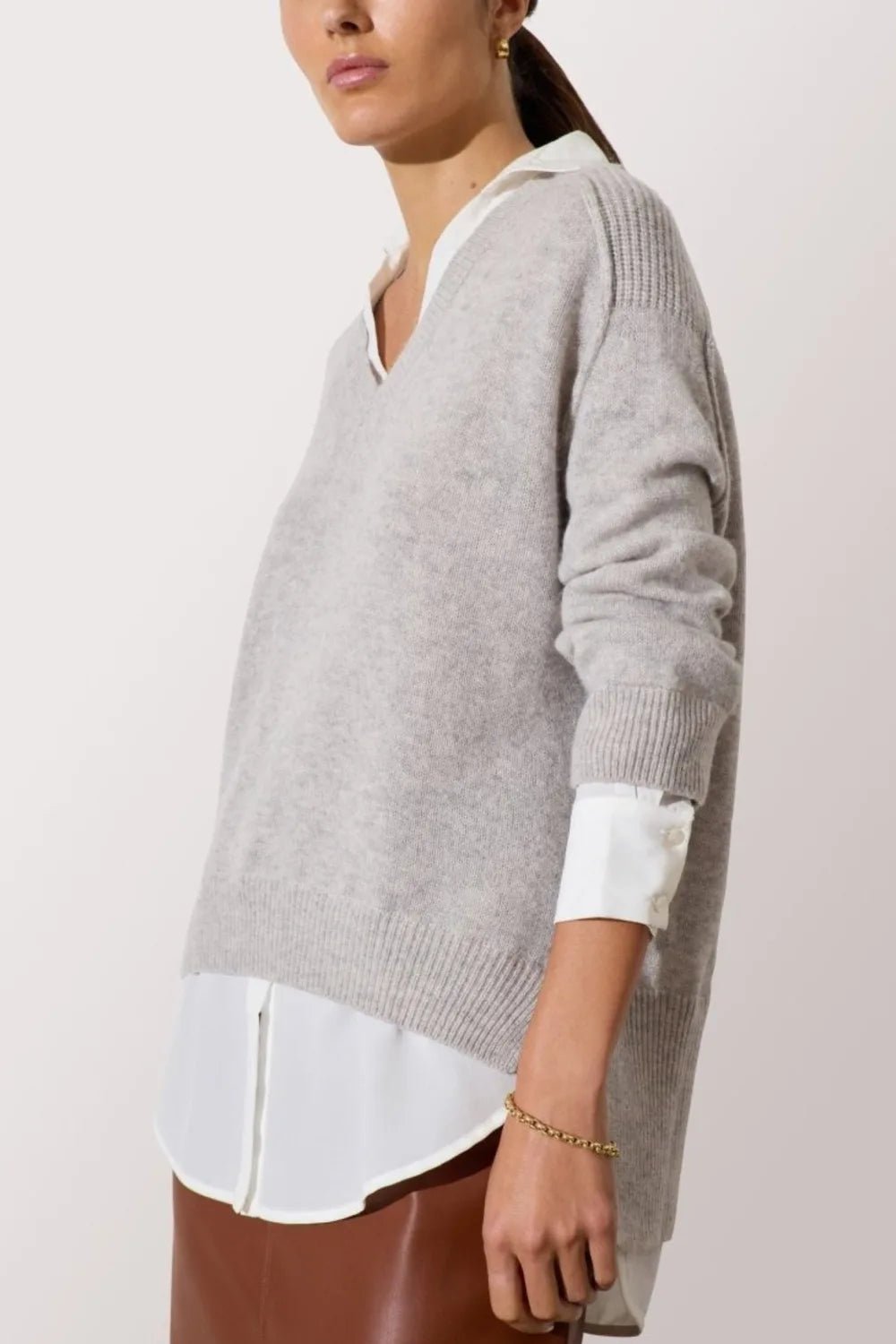 Side view of a grey V-neck layered sweater with a white shirt collar, cuffs, and hem peeking through.