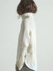 Side view of white layered turtleneck sweater with fringe trim and satin underlayer peeking below hem.