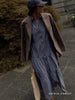 Slate blue tiered Havana maxi dress styled with a brown checked blazer, navy cap, and woven tote on a sidewalk.