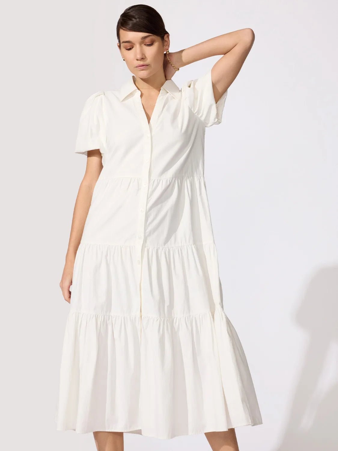 Woman wearing a classy white tiered midi shirtdress with puff sleeves and a button-front placket, hand resting behind her head.